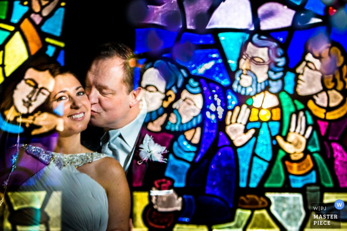 the bride and grooms reflection in a stained glass window Philadelphia wedding photographer creates an image of the bride and grooms reflection in a stained glass window