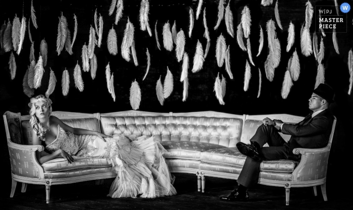 Wisconsin wedding photographer created this portrait of the bride and groom sitting on a long couch while feathers hang behind