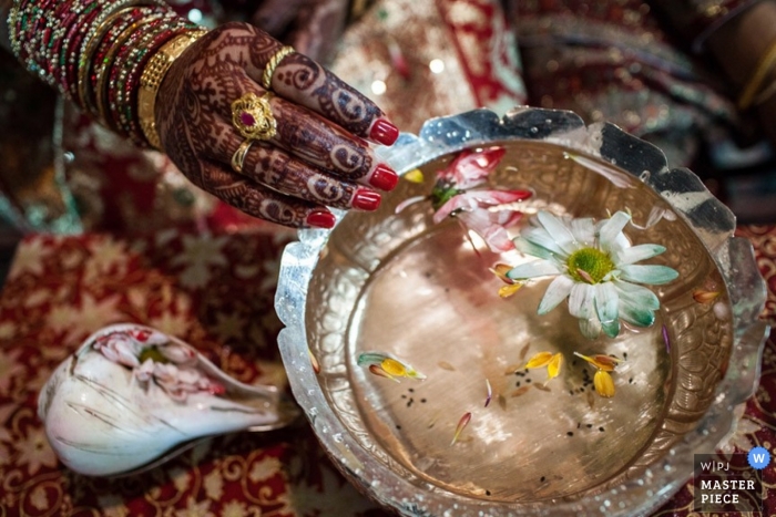 Trouwfotograaf uit Montana maakt deze foto van een met henna getatoeëerde hand die in een kom water met drijvende bloemen doopt