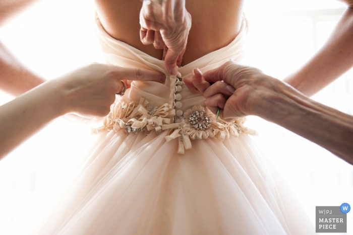 Pennsylvania wedding photographer captured this image of several bridesmaids helping the bride button up the back of her dress before the ceremony 