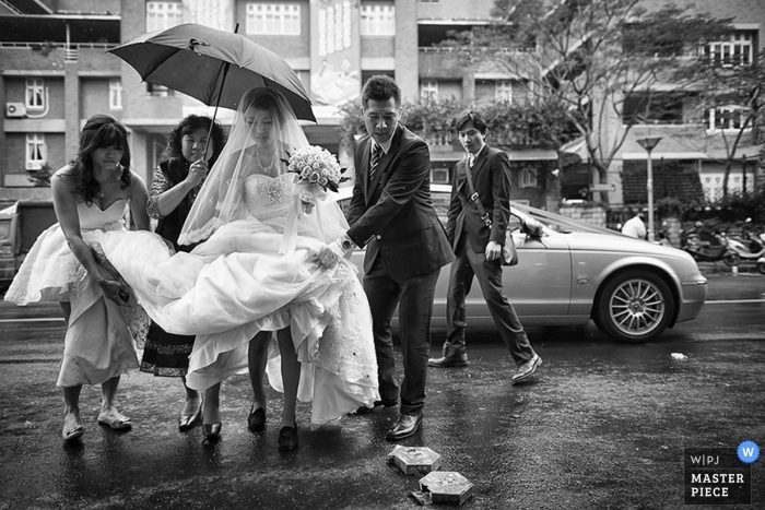Photo by: <a href="https://www.wpja.com/contests/2014-q4-photography-contest/weather/1514226">Shih-Chieh Hsu - Taiwan</a> A bride gets assistance with holding her dress up as she and other wedding guests make their way through a rain storm in this black and white image created by a Taipei wedding photographer
