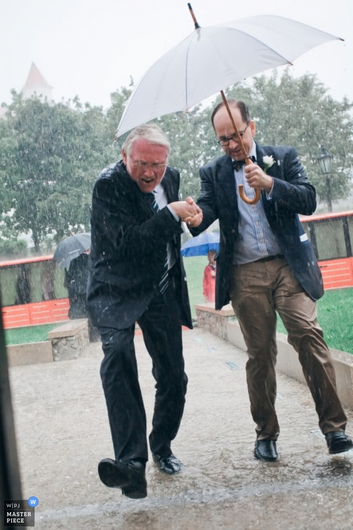 Photo by: <a href="https://www.wpja.com/contests/2014-q4-photography-contest/weather/1537351">Marek Valovic - Austria</a> Vienna wedding photographer gets a shot of a man helping another man into the church in the middle of a rainstorm