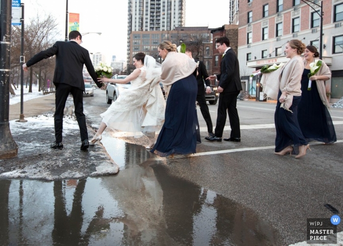 Photo by: <a href="https://www.wpja.com/contests/2014-q4-photography-contest/weather/1584866">Anne Ryan - United States</a> Chicago wedding photographer captured this photo of a bride getting assistance over a large puddle so she didn't ruin her dress