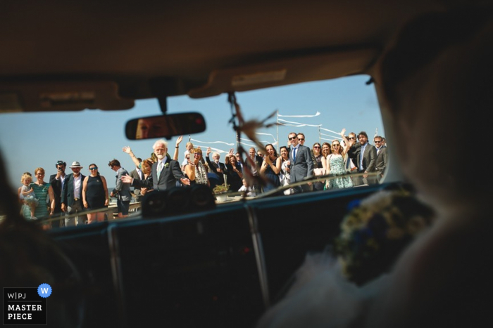 Il fotografo di matrimoni Zuid Holland ha catturato questa immagine degli invitati al matrimonio visti dal sedile posteriore mentre gli sposi si avviano verso la luna di miele