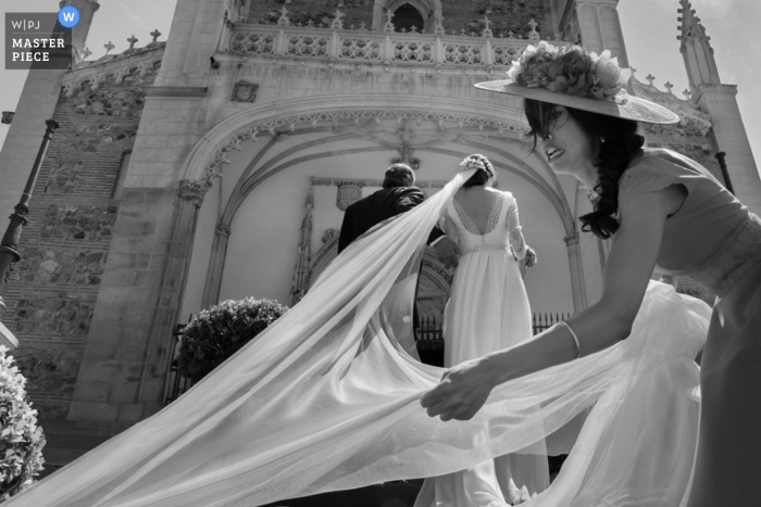 La fotógrafa de bodas de Madrid capturó esta foto en blanco y negro de la novia recibiendo ayuda con el tren en su bata mientras entra a la iglesia