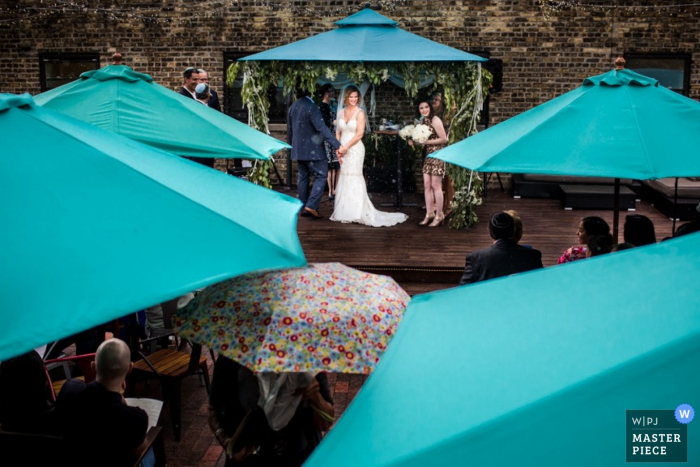 Guests stand under umbrellas as they watch the ceremony in this image created by a Chicago, IL documentary photographer.