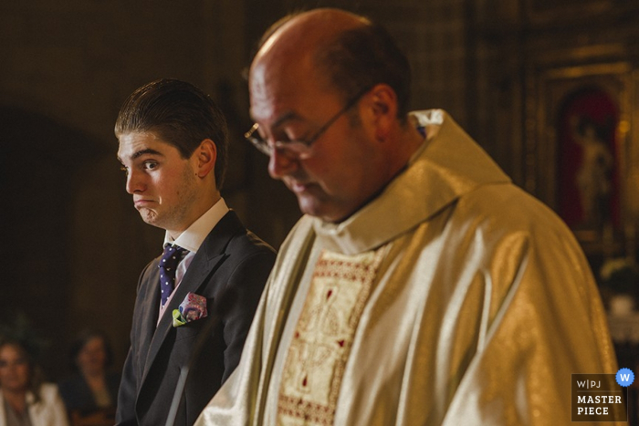 De bruidegom maakt een gezicht terwijl hij naast de priester staat op deze foto van een trouwfotograaf in Madrid, Spanje.