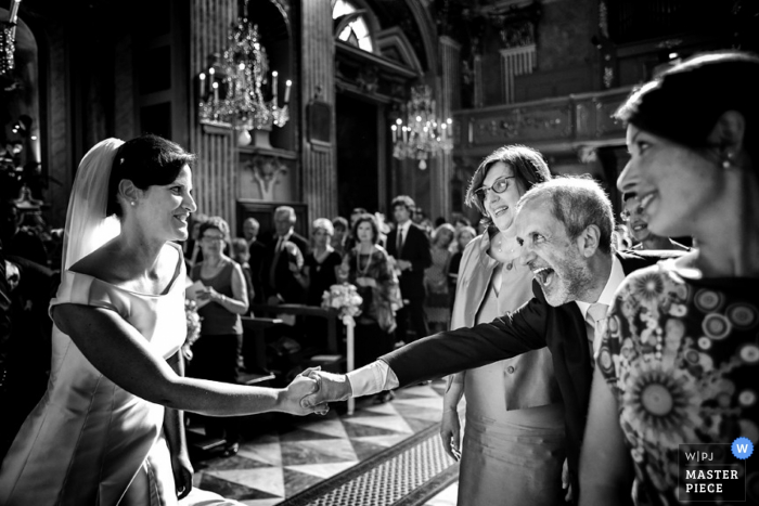 A man leans over to grab the bride's hand after the ceremony in this black and white photo by a Tuscany wedding photographer.