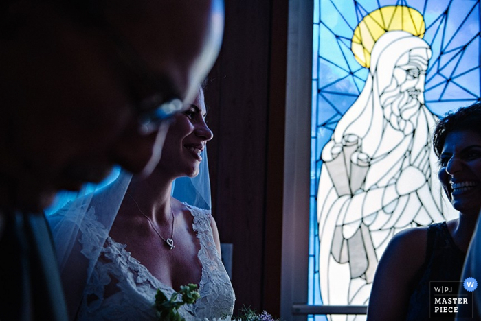 El fotógrafo de bodas de Hudson Valley capturó esta foto de una novia sonriendo mientras el sol brillaba a través de la vidriera junto a ella y le puso un brillo azul en el vestido.