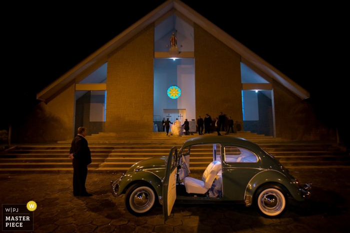 A green Volkswagen waits outside for the bride and groom as they exit the ceremony in this image created by an award-winning Santa Catarina, Brazil wedding photographer A green Volkswagen waits outside for the bride and groom as they exit the ceremony in this image created by an award-winning Santa Catarina, Brazil wedding photographer.