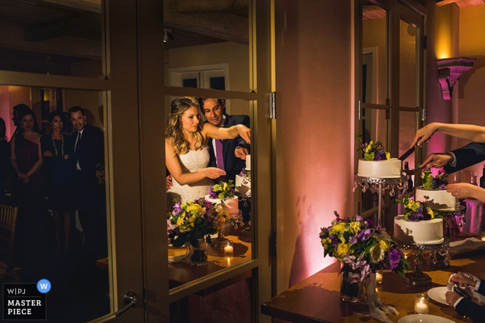 Photo by: <a href="https://www.wpja.com/contests/2015-q2-photography-contest/cake-cutting/1643636">Deborah Coleman - United States</a> The bride and groom are reflected in a mirror as they cut their cake in this photo by a San Francisco, CA wedding photographer.