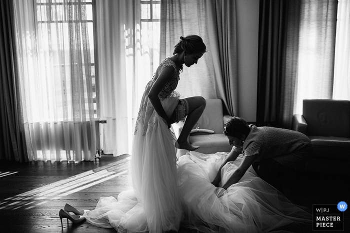 Eine Braut bereitet sich auf ihre Hochzeit vor, während ein Familienmitglied ihr bei ihrem Kleid hilft. Preisgekröntes Bild eines Hochzeitsfotografen aus Sankt Petersburg, Russland.