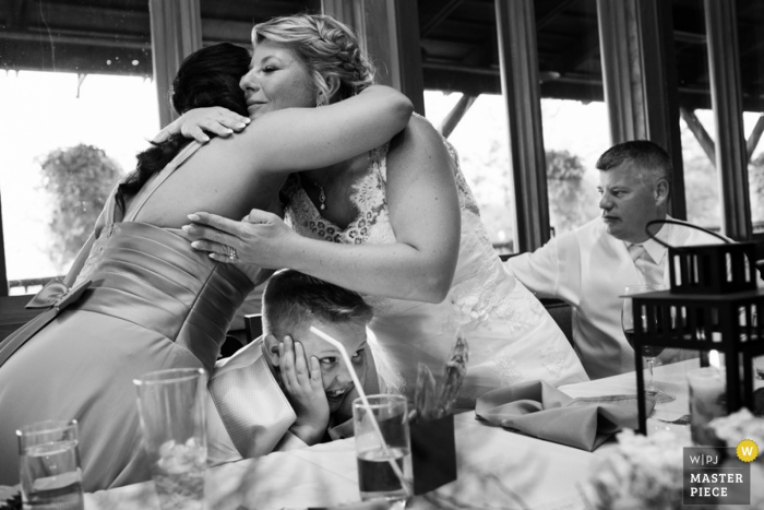 Photo by: <a href="https://www.wpja.com/contests/2015-q4-photography-contest/toastingspeeches/1722431">Jenna Shouldice - Canada</a> Victoria bride and maid of honor hug over little boy at the reception | British Columbia wedding photography