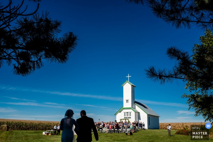 Photo par: <a href="https://www.wpja.com/contests/2015-q4-photography-contest/ceremony/1729271"> Janine Cooper - États-Unis </a> Mariée Omaha et son père marchant vers la cérémonie en plein air à l'église de pays | Nebraska photo de mariage