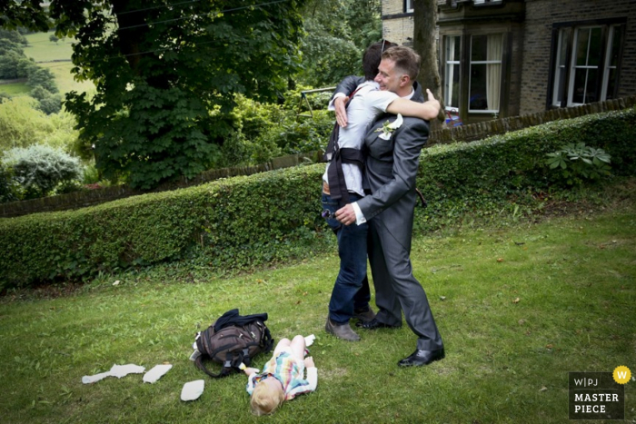 Invitado londinense abraza al novio antes de cambiar a su bebé | Foto de reportaje de boda de Inglaterra