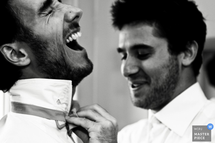 Paris groom laughs as he gets help with his tie before the wedding |  France wedding photojournalism