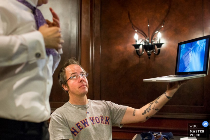 Wedding photograph of groomsman holding laptop computer while helping tie during the getting ready in New Jersey 