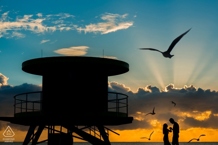 São Paulo pré-casamento Fotos na praia perto da torre de salva-vidas. Belo pôr do sol, nuvens e pássaros.