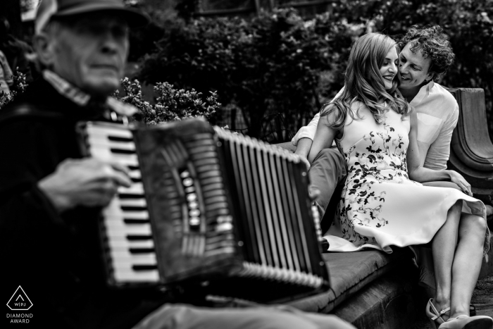 Photo by: <a href="https://www.wpja.com/photos/diamond-award-top-wedding-engagement-photographer/2172781">Curtis Moore - Canada Wedding Photographer</a> Black and white engagement portrait of couple sitting with a man playing the accordion | Winnipeg wedding photographer
