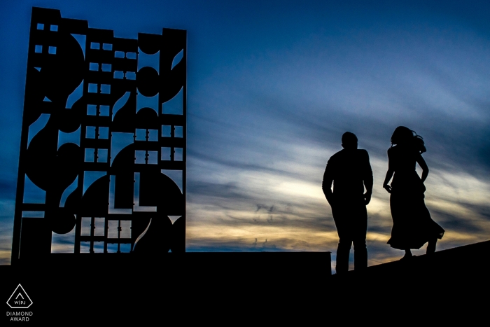 Photographie d'engagement de New York City | oeuvre et couple se découpent en noir sur un ciel bleu dramatique