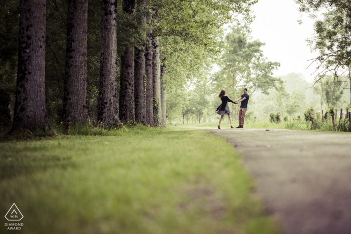 Photo de: <a href="https://www.wpja.com/photos/diamond-award-top-wedding-engagement-photographer/2189796"> Romuald Goudeau - Photographe de mariage en France </a> Portraits de fiançailles Pays de la Loire | couple nouvellement fiancé fait une promenade ludique sur le sentier à côté de la forêt avec de grands arbres
