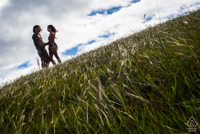 Madrid pre-wedding portraits of a couple in a grassy field with a tilted horizon and a blue sky with clouds Madrid pre-wedding portraits of a couple in a grassy field | tilted horizon with a blue sky and clouds