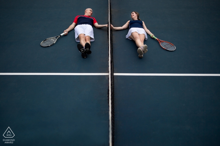 Foto: <a href="https://www.wpja.com/photos/diamond-award-top-wedding-engagement-photographer/2196696"> Mari Harsan - Hochzeitsfotograf aus den Vereinigten Staaten </a> Washington DC, Match Game - liebevolle Paare des Tennis liegen auf dem Gerichtshändchen durch das Netz während ihres Vorhochzeitsporträts