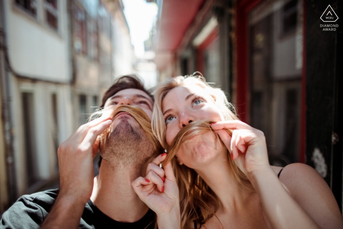 Humorous engagement portrait of this coupled using her hair to create mustaches for both in Portugal