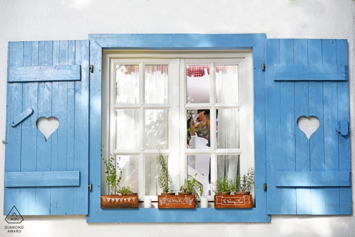 Window in the village with planter boxes and shutters framed this Romanian couple for their engagement portrait