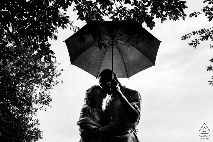 Portrait de fiançailles Nouvelle-Aquitaine sous les arbres et abrité par un parapluie