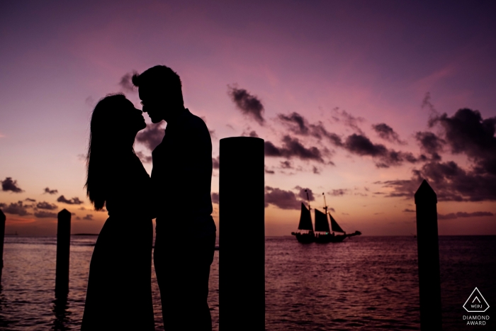 Photo by: <a href="https://www.wpja.com/photos/diamond-award-top-wedding-engagement-photographer/2291121">Julie Ambos - Key West Florida engagement pictures of a couple silhouetted with a sailboat in the distance | Key West photographer pre-wedding photo shoot session