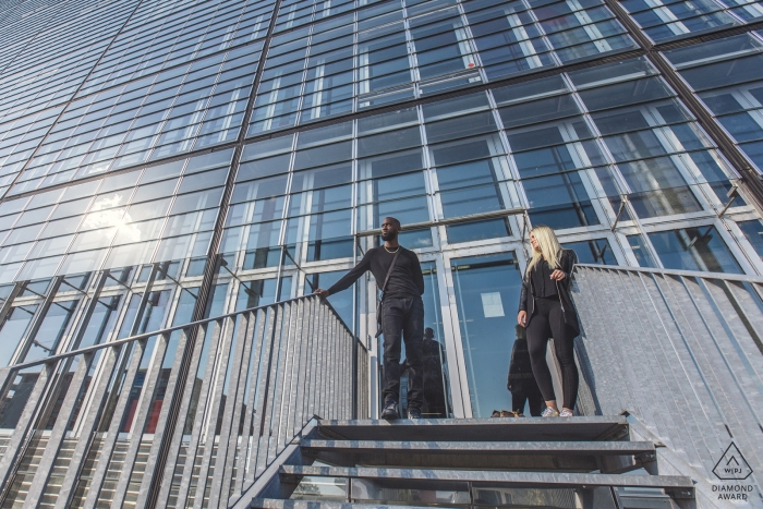 Mariage urbain du Haut-Rhin: portrait d'un couple dans un escalier avec un immense bâtiment en verre | Séance de photographe pré-mariage Grand Estate