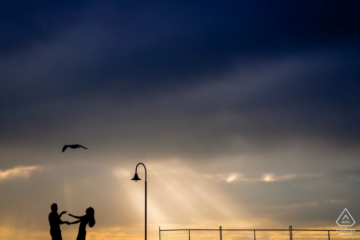 Vietnam engagement photos of a couple at the ocean with a seagull and lamp post  | Ho Chi Minh photographer pre-wedding portrait session