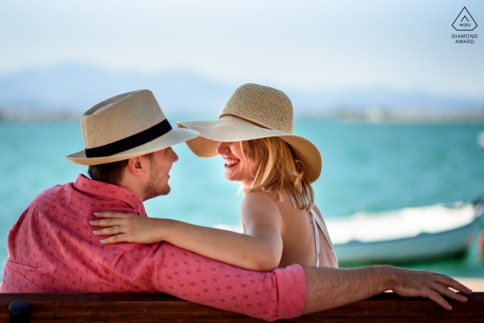 Photo by: <a href="https://www.wpja.com/photos/diamond-award-top-wedding-engagement-photographer/2330036">Corina Oghina - Brighton East Sussex Girl smiling at her fiancee with sun hats at the beach during engagement shoot | East Sussex England