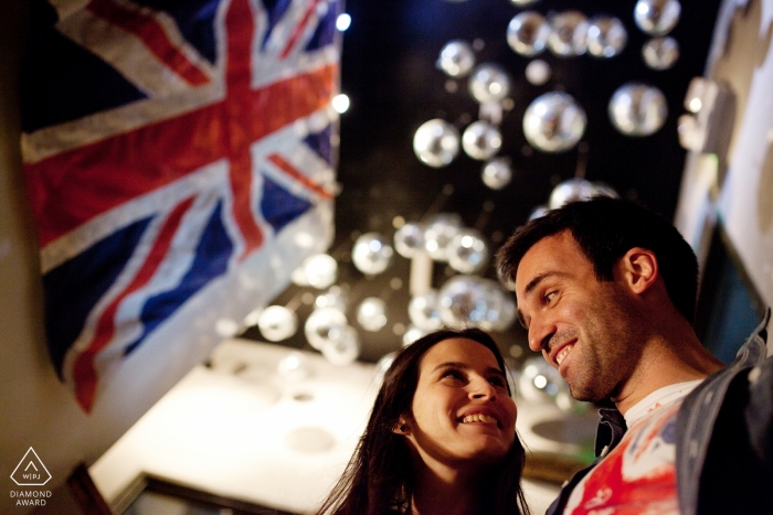 The happy couple smiled brightly while a flag waved and captured in a stunning low angle engagement photo Braga engagement photos of a couple with flags and lights | Portugal photographer pre-wedding portrait session