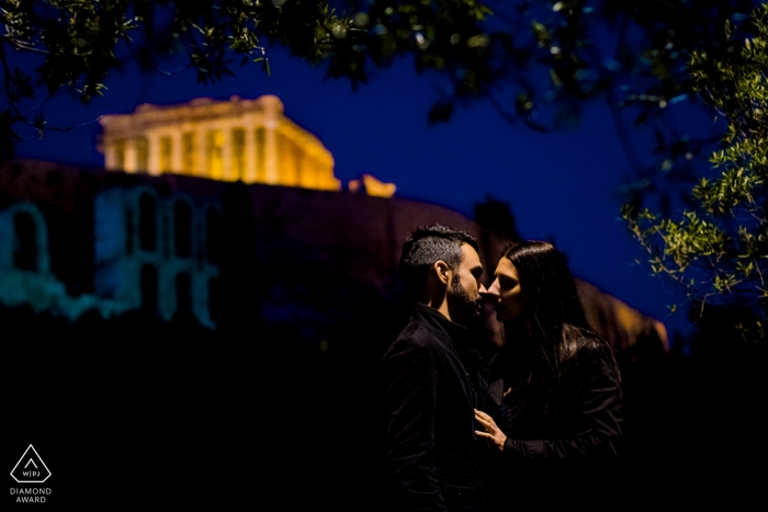 Verlobungsfotos vor der Hochzeit in Athen von einem Paar, das sich nachts unter Straßenbeleuchtung küsst | Fotosession für Paare