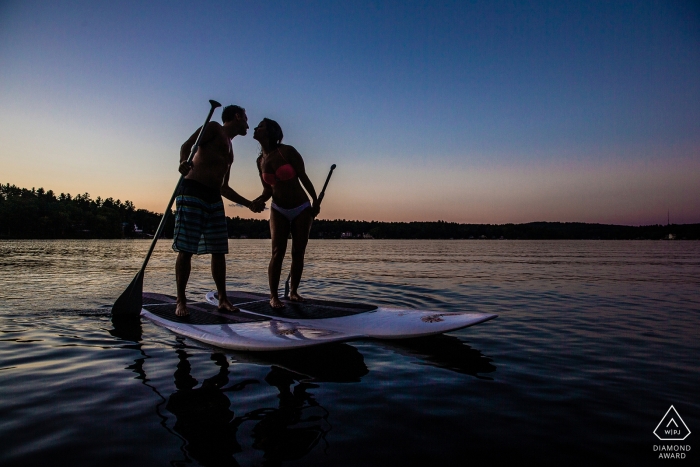 订婚的夫妇在paddleboards在水在日落在Windham，NH。