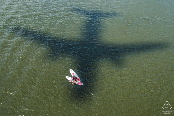 Fotografía de compromiso de boda SUP en District Of Columbia con la sombra de un avión en el agua Fotografía de compromiso de boda SUP en District Of Columbia con la sombra de un avión en el agua