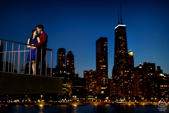 An Illinois engaged couple perched happily on the balcony railing overlooking Chicago