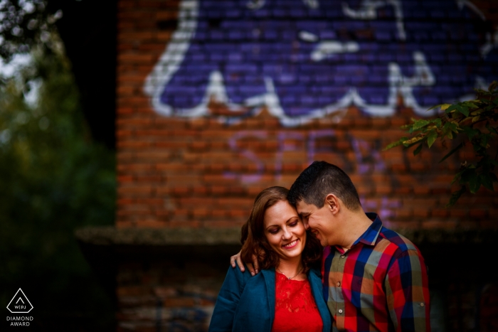 București couple stand embraced and backed by a red brick wall