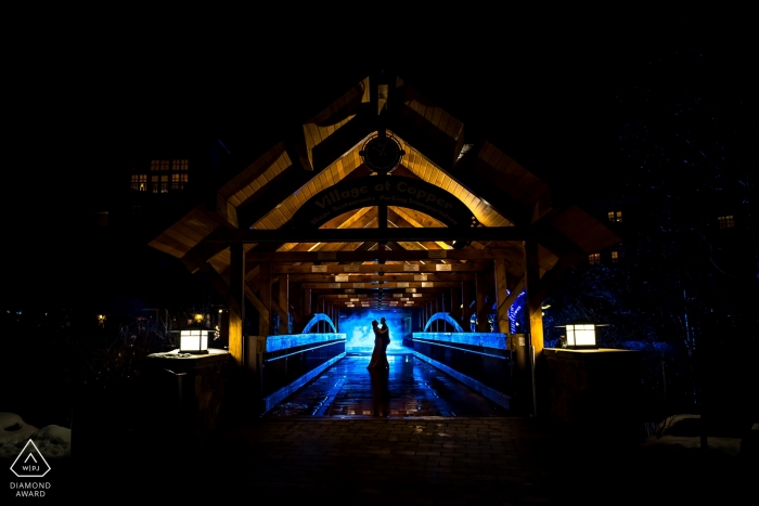 Colorado couple standing on a pedestrian bridge at a ski resort between the condos and the chair lifts