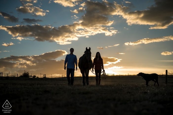 Boulder couple walking as ranchers, silhouetted against clouds in the sky