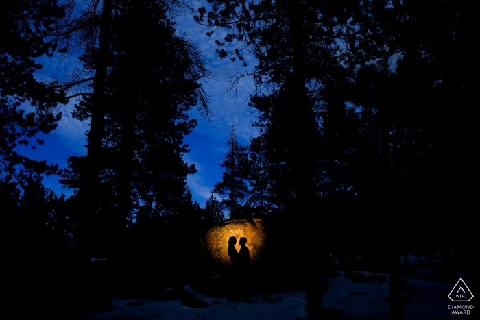 Colorado couple embraced in the dark woods, illuminated by the last rays of sun