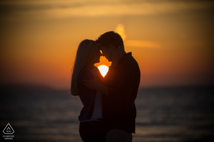 Fotosession des verlobten Paares auf den Kanalinseln am Meer mit orangefarbenem Sonnenuntergang