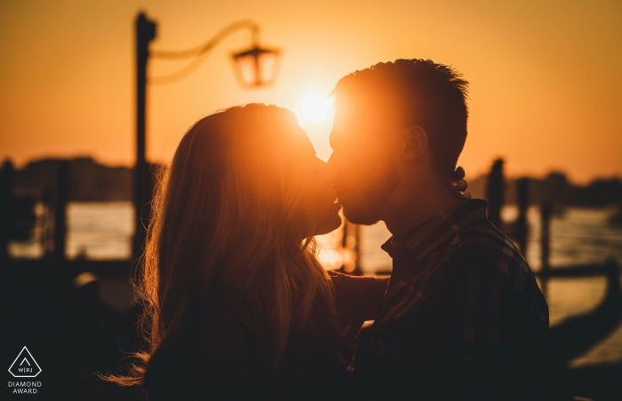 Um casal Venezia com um pôr do sol laranja no único poste de luz