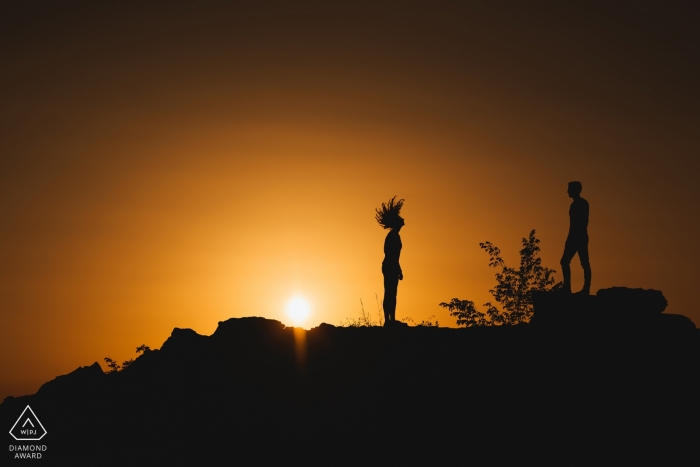 A sun seeking Slovenia couple stands silhouetted against an orange sky