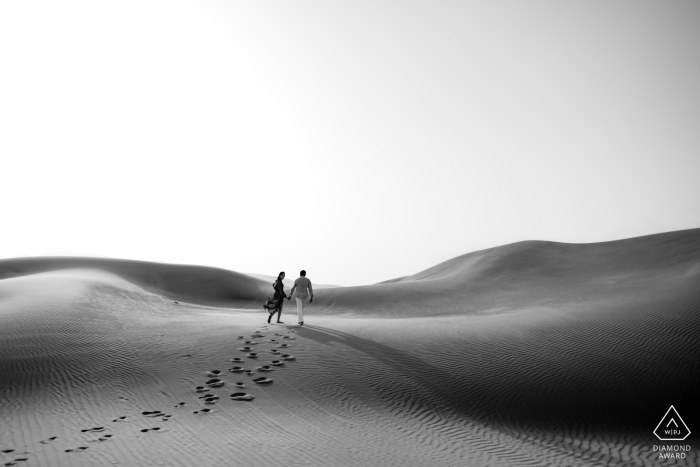 Foto pré-casamento de Dubai, Emirados Árabes Unidos, de casal caminhando pelas dunas de areia em foto BW