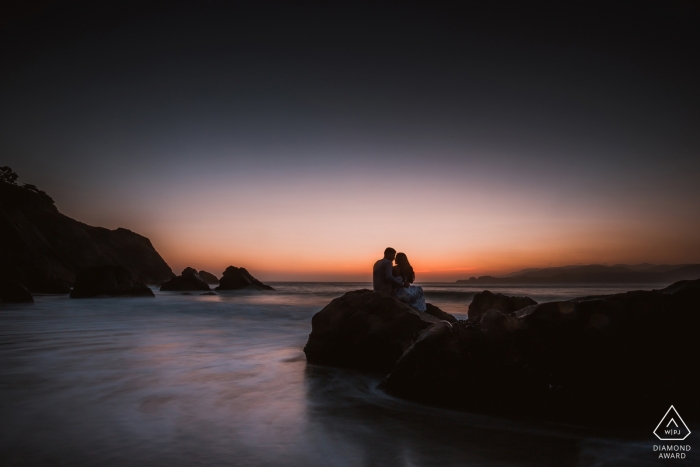 Casal da Califórnia senta-se no topo de uma rocha, olhando para o horizonte ao pôr do sol