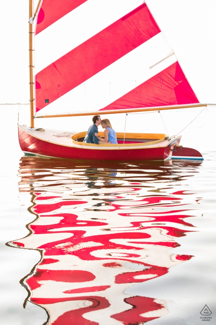 Couple du Massachusetts dans leur petit voilier, avec sa voile rayée rouge et blanche