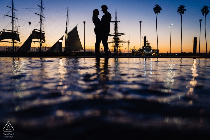 Ein Paar aus San Diego posiert am Yachthafen bei Sonnenuntergang zwischen Palmen und Segelbooten